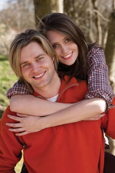 Attractive young couple cuddling out doors. They are both looking at the camera