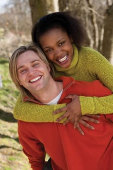 Attractive young couple cuddling out doors. They are both looking at the camera