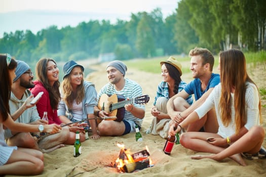 Big company of friends sitting around campfire in natural environment