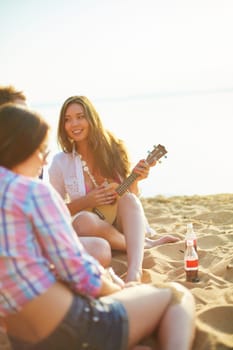 Pretty girl with guitar looking at her friend while sitting on sandy beach
