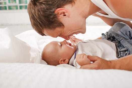 Young smiling father with his nine months old son on the bed at home on white home background