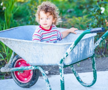 Portrait of 1 year old baby boy playing with a wheel barrow.