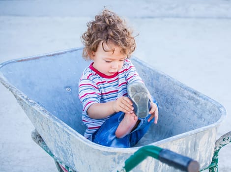 Portrait of 1 year old baby boy playing in a wheel barrow.