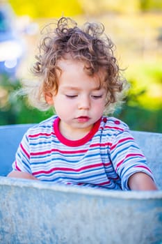 Portrait of 1 year old baby boy playing with a wheel barrow.