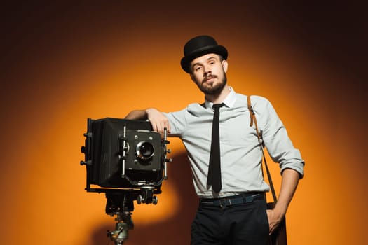 Young  positive man in hat as photographer with retro camera on an orange background