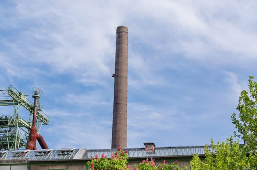 Large factory chimney of an old factory in front of blue sky.