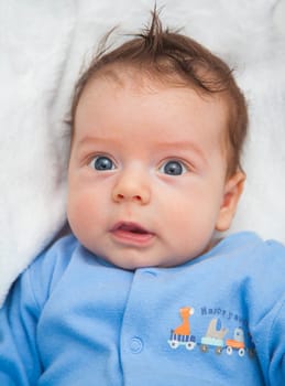 Portrait of a 2 moths old baby dressed in blue on a white blankie.