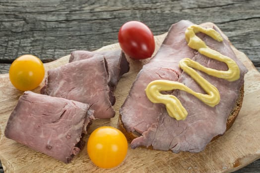 Bread with roast beef and mustard on a wooden board