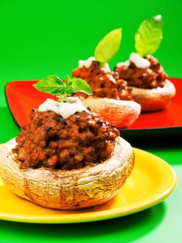Stuffed mushrooms with meat and mozzarella decorated with fresh basil, izolated on green background