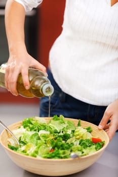 Young woman making salad in the kitchen and pooring olive oil