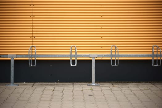 A series of bicycle stands are mounted in front of a distinctively coloured corrugated iron facade.