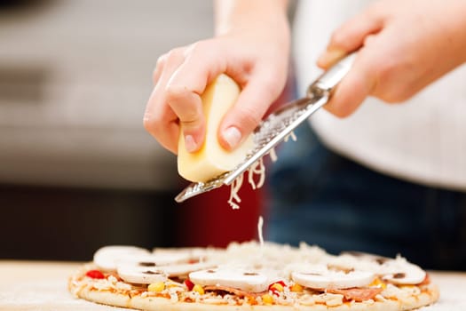 Young woman preparing homemade pizza - greating cheese