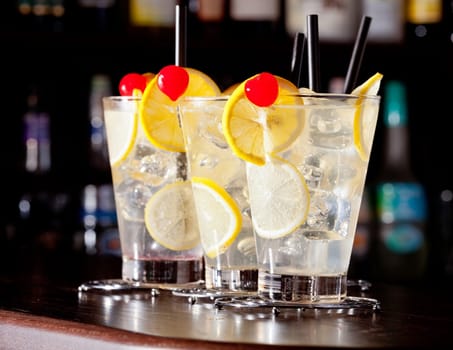 The Tom Collins is a Collins cocktail made from gin, lemon juice, sugar and carbonated water. First memorialized in writing in 1876 by &quot the father of American mixology&quot Jerry Thomas, this &quot gin and sparkling lemonade&quot drink typically is served in a Collins glass over ice. On the photo - four glasses of Tom Collins cocktail at a bar.