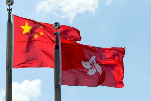Hong Kong and Peoples Republic of China Flags Flying Side by Side Against Blue Sky