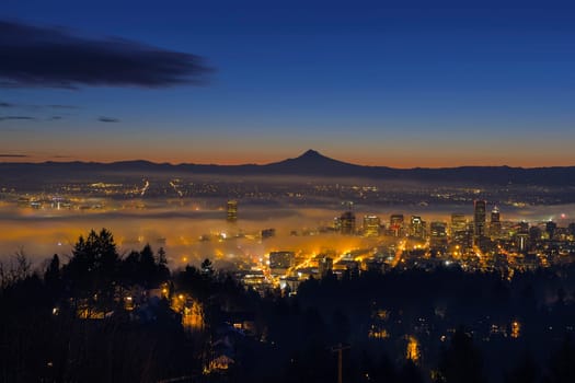 Thick Fog Rolling at Dawn over cityscape of downtown Portland Oregon with city lights and silhouette of Mt Hood
