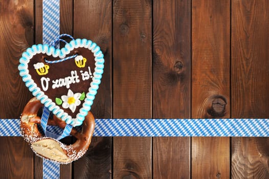 Greetings from Oktoberfest - original Bavarian Laugenbrezel with Oktoberfest gingerbread heart in front of a wooden wall