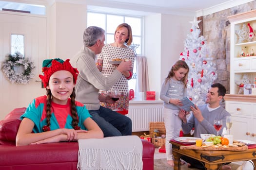 Three Generation Family at Christmas Time. Young Girl is looking at the Camera and Smiling while the family chat in the background.