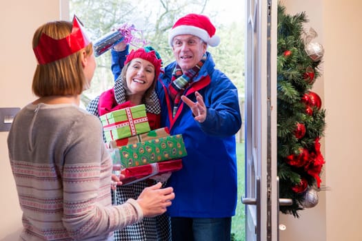 Senior couple delivering presents at Christmas time. They are both smiling and are holding Christmas gifts.