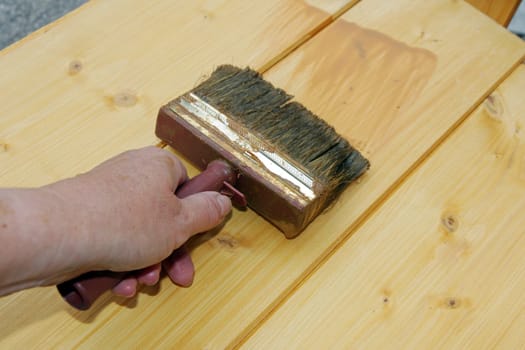 A woman strokes wood protection glaze on boards with a brush