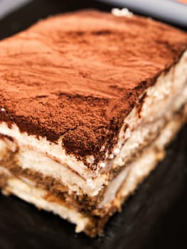 Tiramisu cake in a black plate, close up