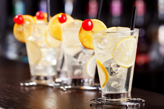 The Tom Collins is a Collins cocktail made from gin, lemon juice, sugar and carbonated water. First memorialized in writing in 1876 by &quot the father of American mixology&quot Jerry Thomas, this &quot gin and sparkling lemonade&quot drink typically is served in a Collins glass over ice. On the photo - four glasses of Tom Collins cocktail at a bar.