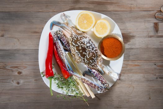 Above view raw blue crab and ingredients ready to cook, on white plate.