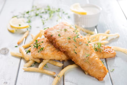 Fish and chips. Fried fish fillet with french fries on bright wooden background. Fresh cooked with hot smoke.