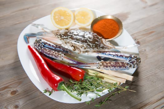 Raw blue crab and ingredients ready to cook, on white plate.