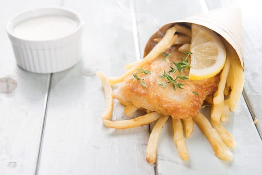 Fish and chips. Fried fish fillet with french fries wrapped by paper cone, on wooden background. Fresh cooked with hot smoke.