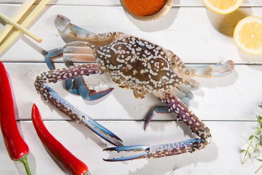 Above view raw blue crab and ingredients ready to cook, on bright wooden background.