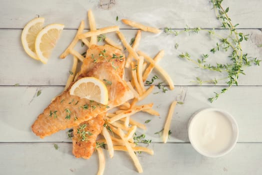 Fish and chips. Top view fried fish fillet with french fries on wooden background, vintage tone.