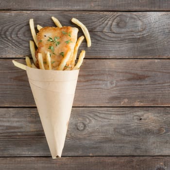 Fish and chips. Top view fried fish fillet with french fries wrapped by paper cone, on wooden background.