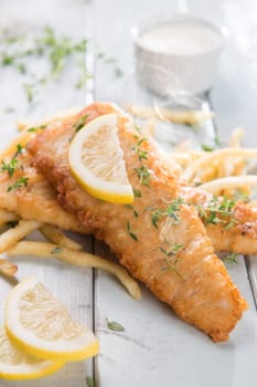 Fish and chips. Fried fish fillet with french fries on bright wooden background. Fresh cooked with hot steams smoke.