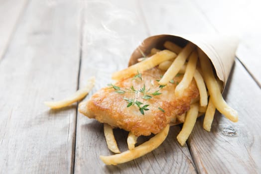 Fish and chips. Fried fish fillet with french fries wrapped by paper cone, on wooden background.