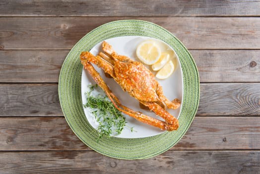 Top view cooked delicious hot and spicy sauce blue crab on white plate, at wooden background. Fresh cook with hot smoke steams.
