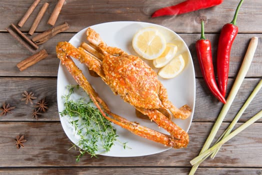 Top view cooked delicious hot and spicy sauce blue crab on white plate with ingredients, at wood background. Fresh cook with hot smoke steams.