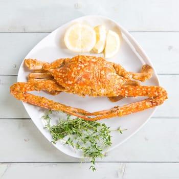 Above view cooked delicious hot and spicy sauce blue crab on white plate, at bright wooden background. Fresh cook with hot smoke steams.
