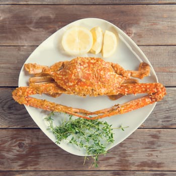 Top view cooked delicious hot and spicy sauce blue crab on white plate, at wood background in vintage style. Fresh cook with hot smoke steams.