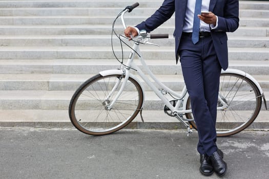 Businessman with cellphone standing by bicycle