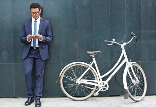 Handsome employee with cellphone standing by wall of modern building with bicycle near by