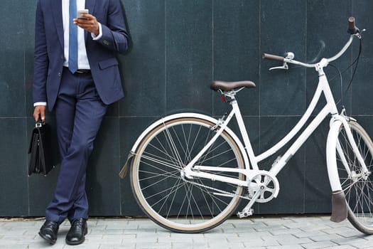 Close-up of modern businessman with cellphone standing by wall of modern building with bicycle near by