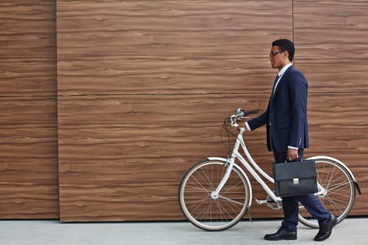 Businessman with briefcase and bicycle walking along wooden wall