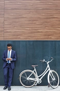 Handsome businessman reading sms while standing by modern building with bicycle near by