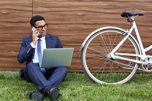 Elegant businessman with laptop speaking on the phone against wooden wall
