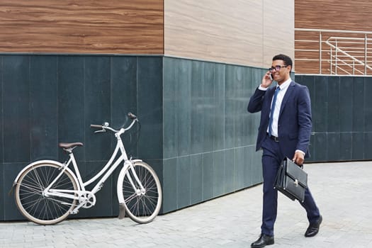 Young businessman with cellphone passing by modern building and calling