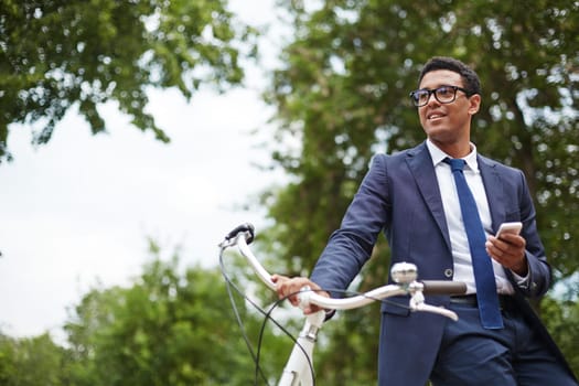 Young businessman with cellphone and bicycle having break in park