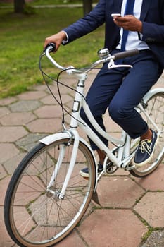 Modern and active businessman with cellphone riding bicycle in park