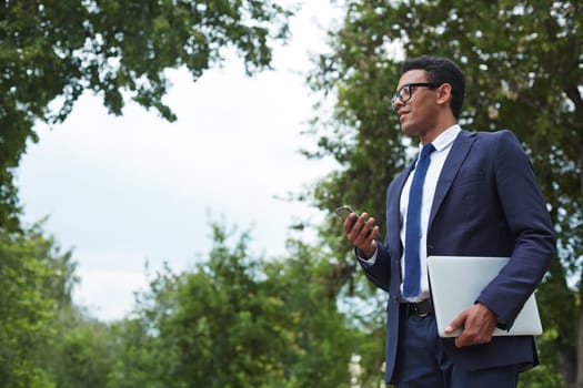 Handsome businessman with digital tablet and cellphone standing in park