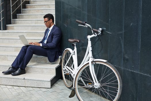 Young employee typing on stairs by modern building