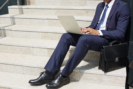 Contemporary businessman typing on laptop keypad while sitting on stairs outdoors